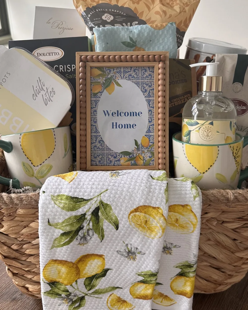 Welcome home basket with a lemon-print tea towel, framed welcome sign and lemon-themed mugs